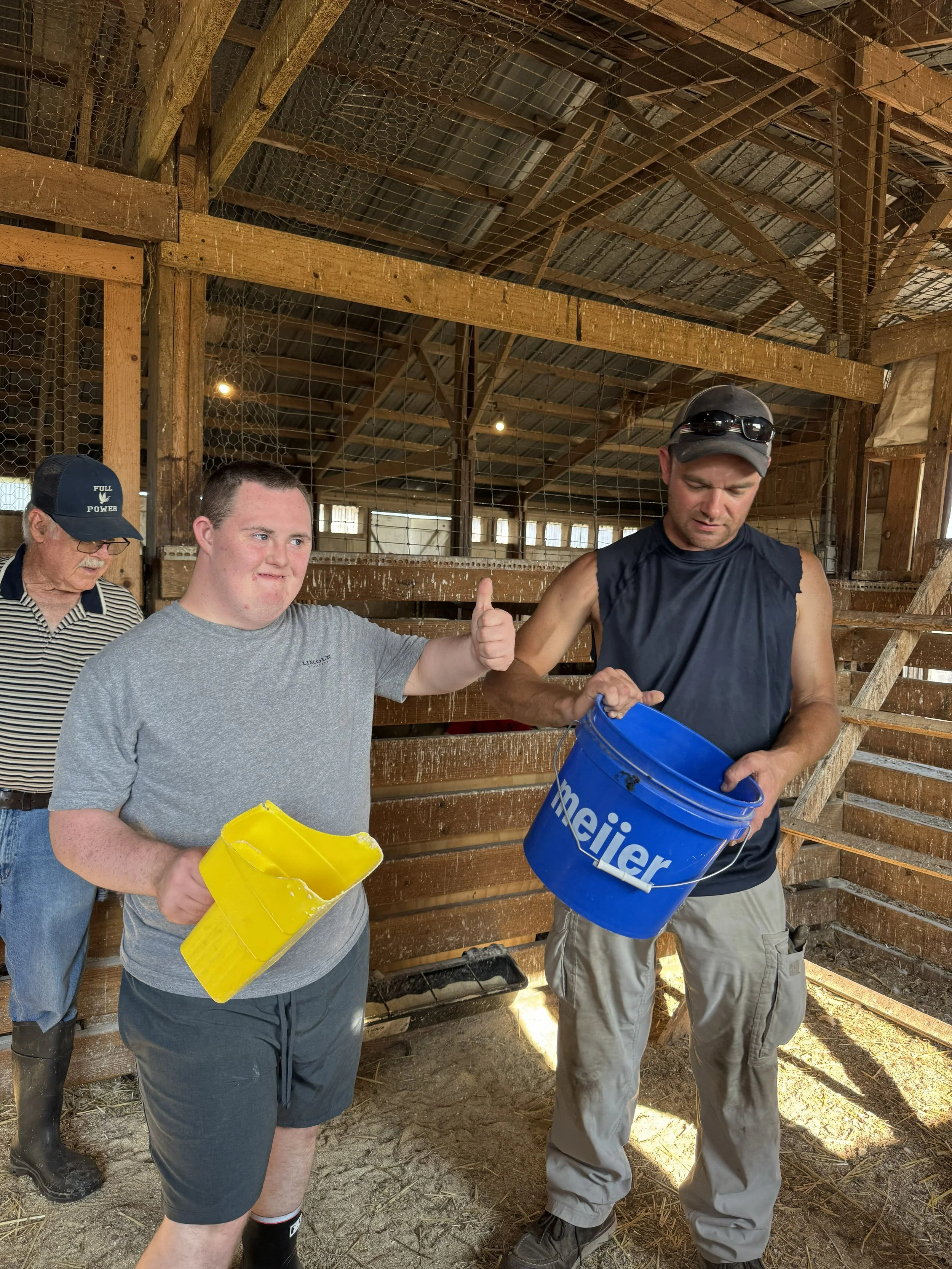 Chance gives a thumbs up while standing with a local farm owner and helping feed barn animals.