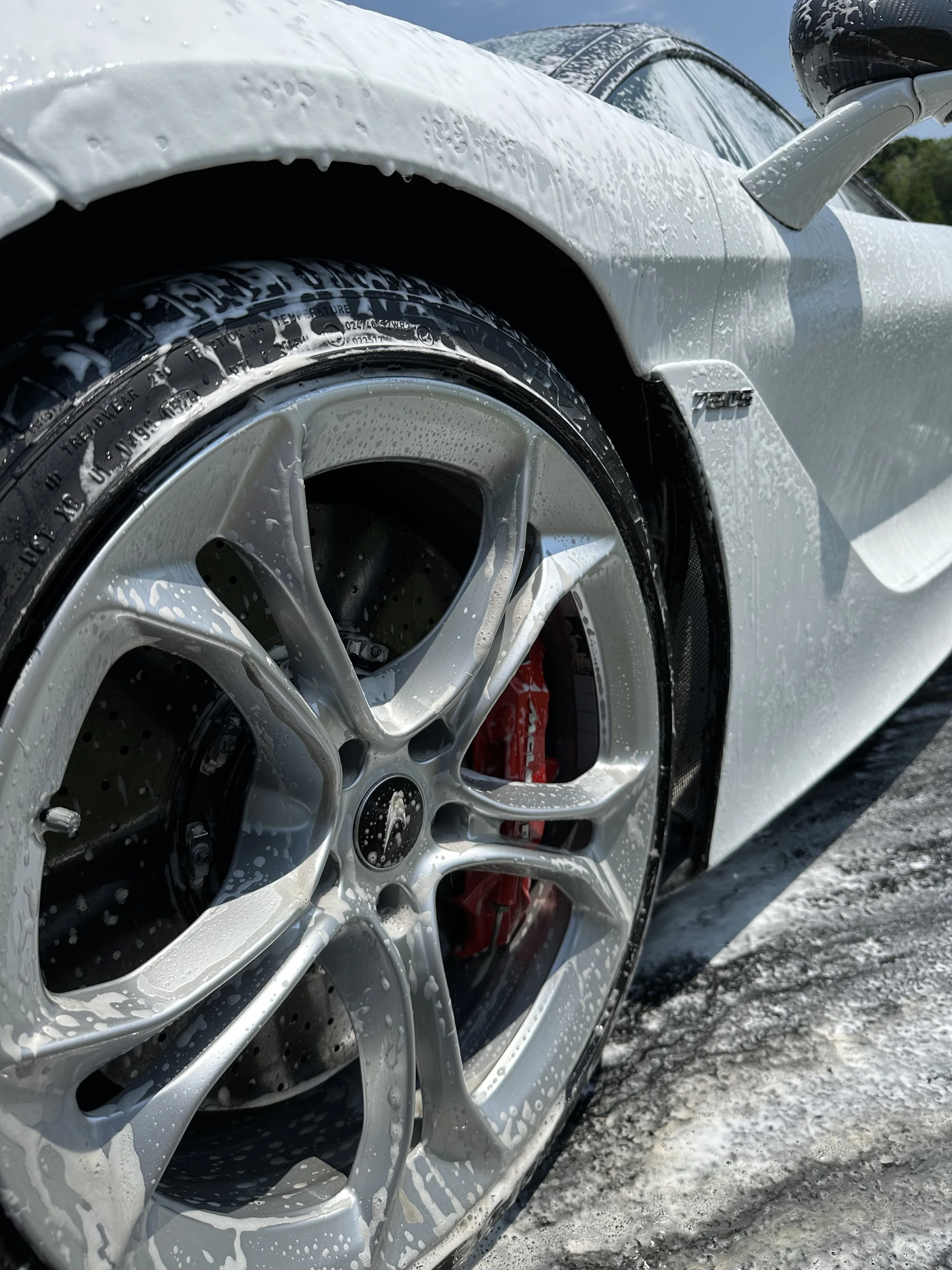 Close-up of a white sports car being washed, with soap suds on the body, wheel, and tire.