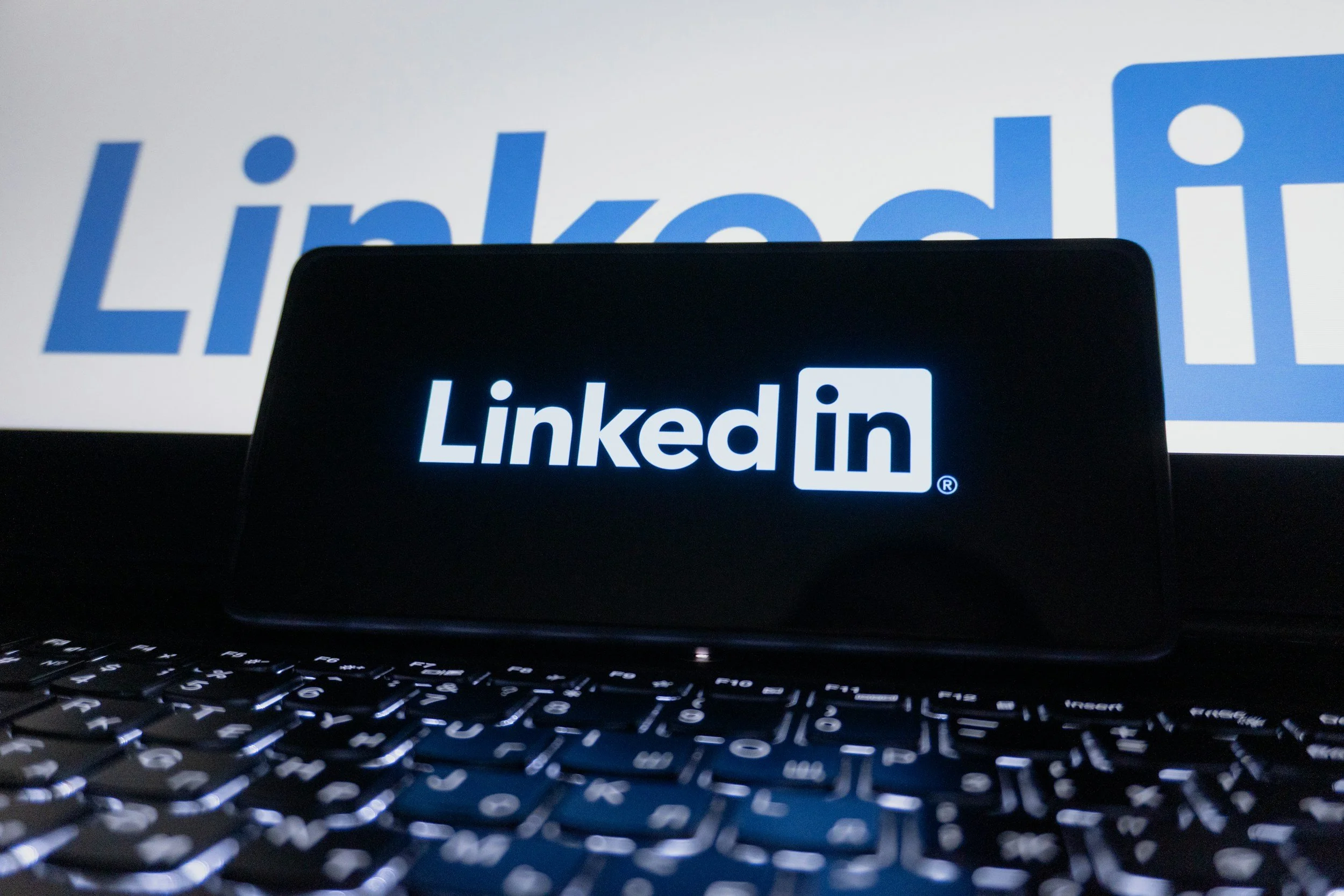 A computer screen displaying the LinkedIn logo with a finger pointing to it, and a keyboard in the foreground.