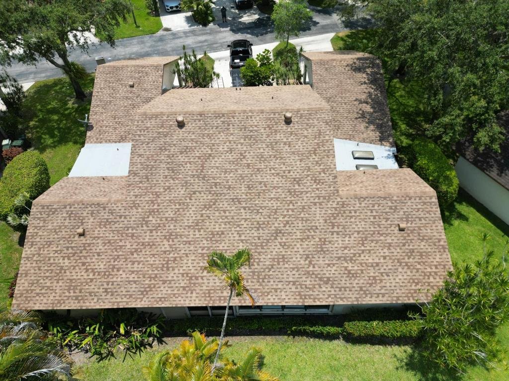 Aerial view of a house with a wooden shingle roof surrounded by greenery, trees, and a parking area with cars.