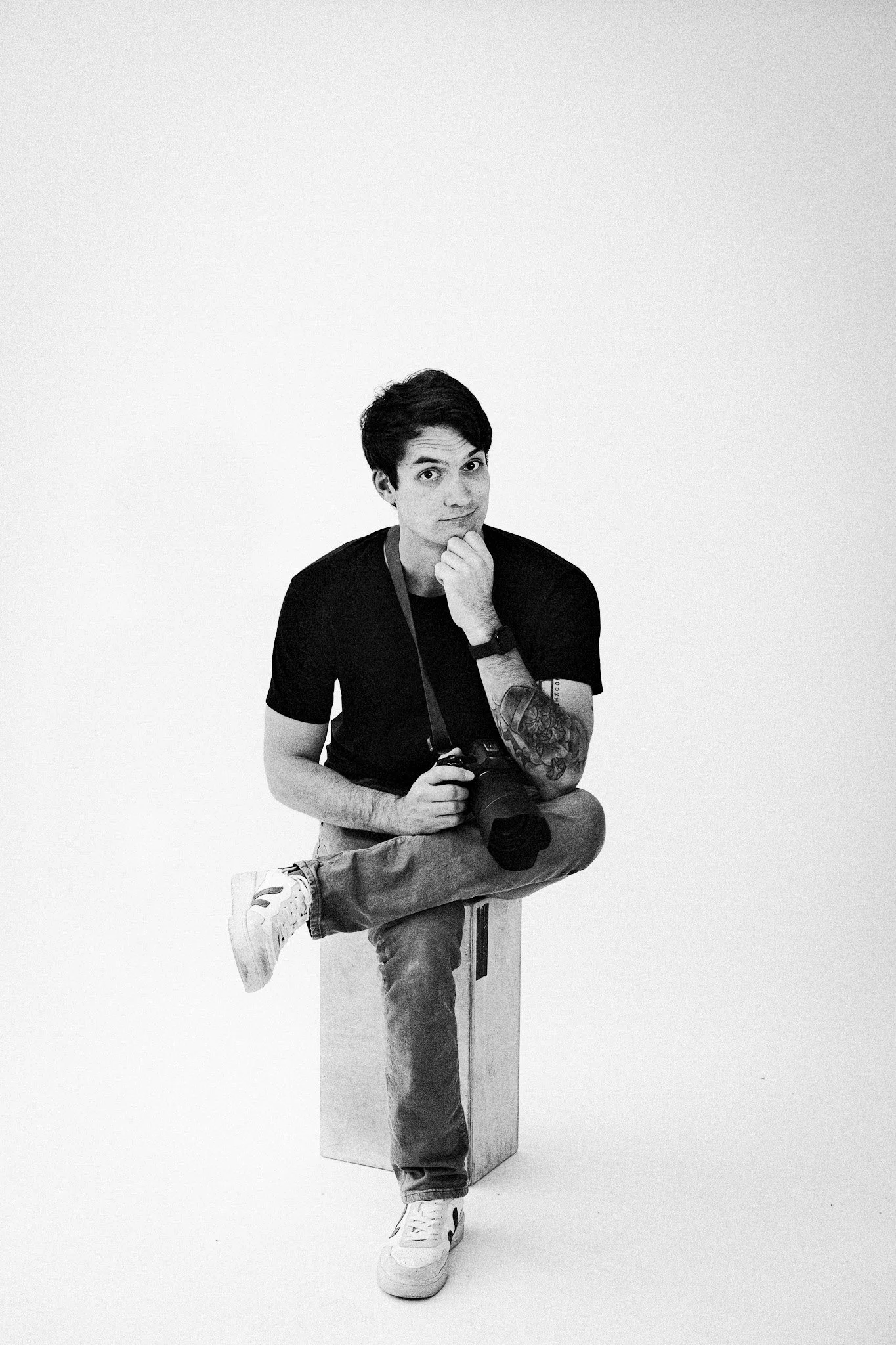Portrait of Andy Bodemer sitting on an apple box with his legs crossed, holding a camera. Photo by Carlos Guzman, Salt Lake City Utah, 2025