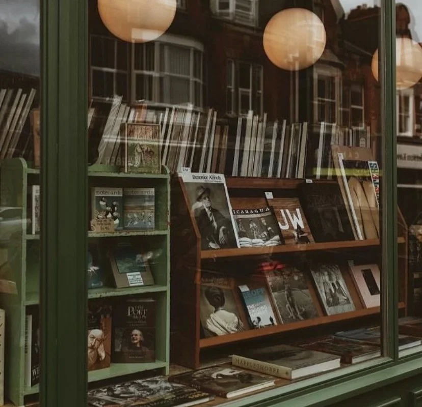 View of a bookstore window with shelves of books and magazines, and round paper lanterns reflecting in the glass.