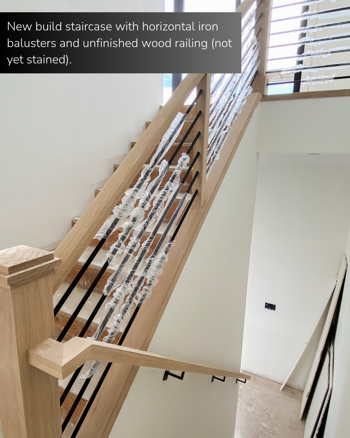 New build staircase with horizontal iron balusters and unfinished wood railing (not stained).
