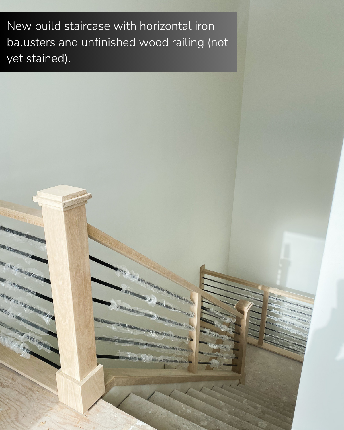 New build staircase with horizontal iron balusters and unfinished wood railing (not yet stained). 