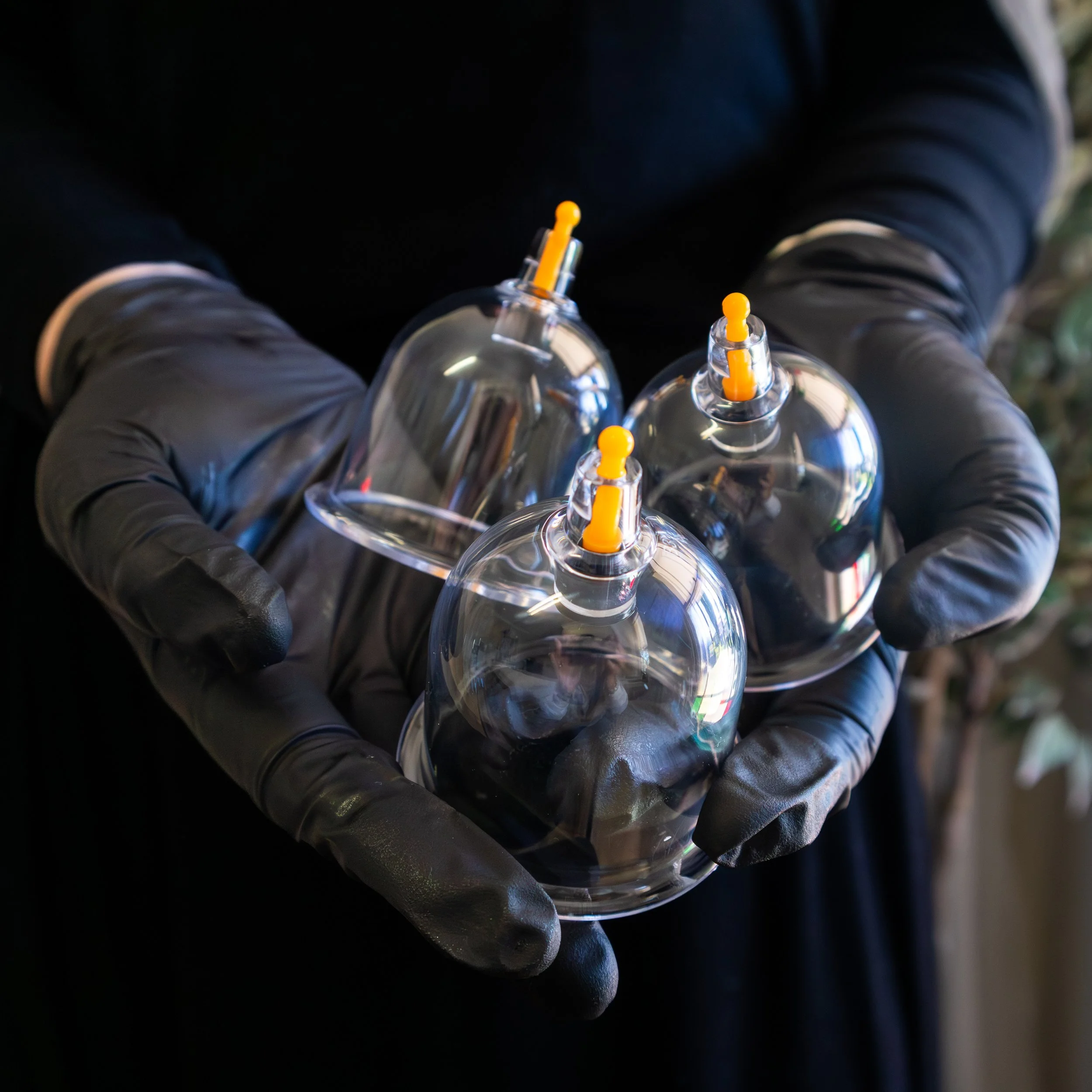 Person wearing black gloves holding three clear plastic ornaments with orange plastic hooks.