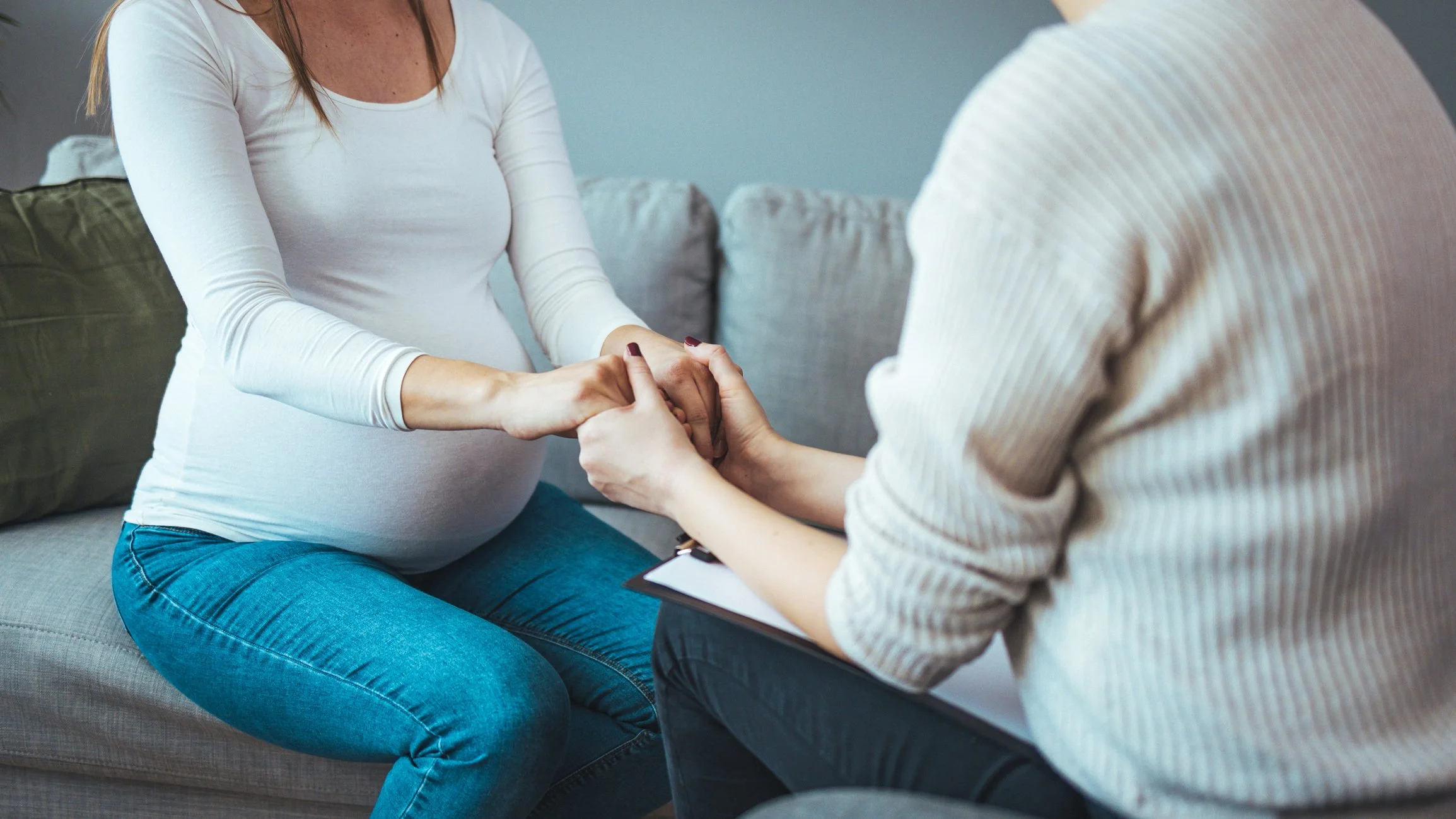 A pregnant woman holding hands with a therapist during a therapy session.