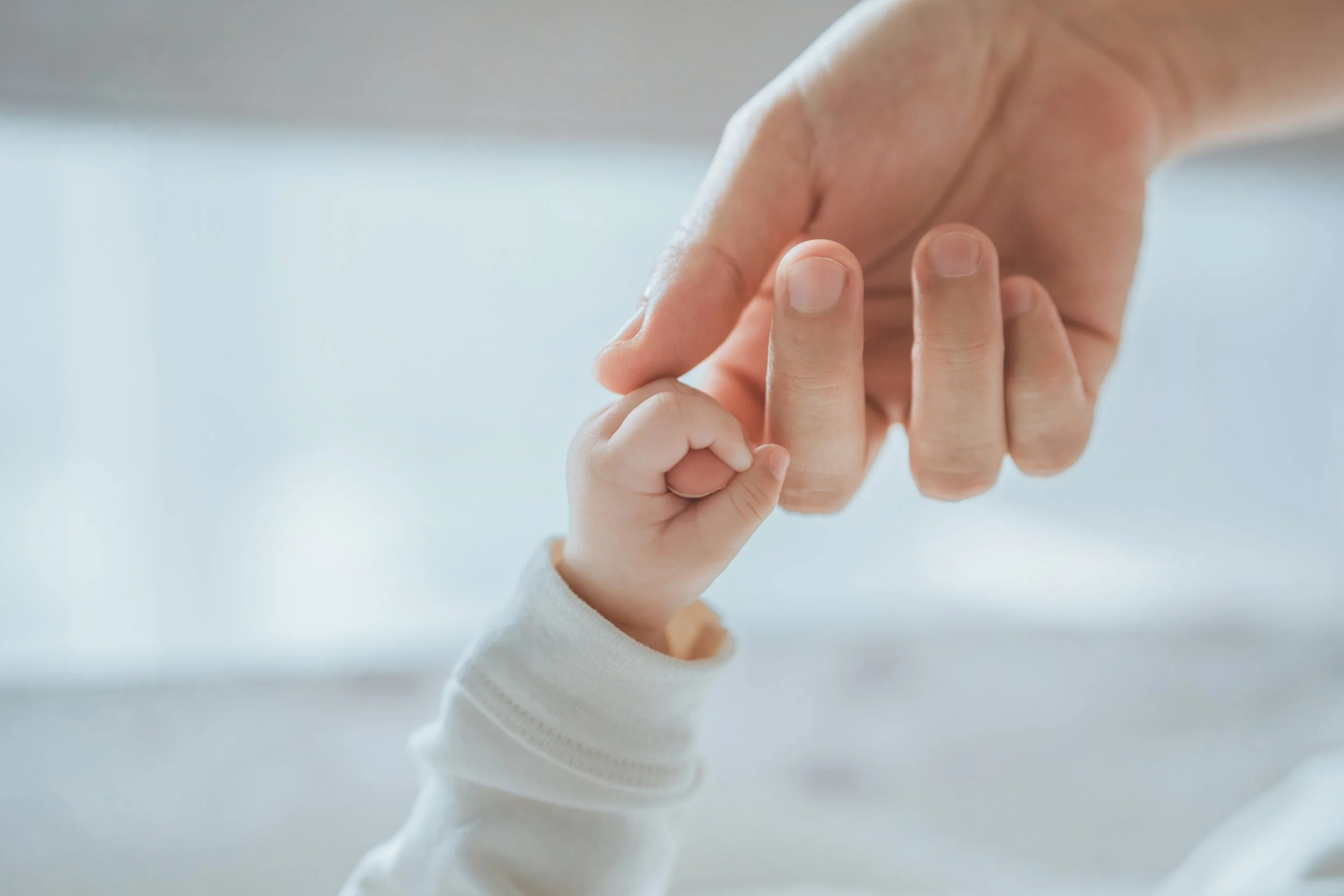An adult hand gently holding a child's tiny hand.