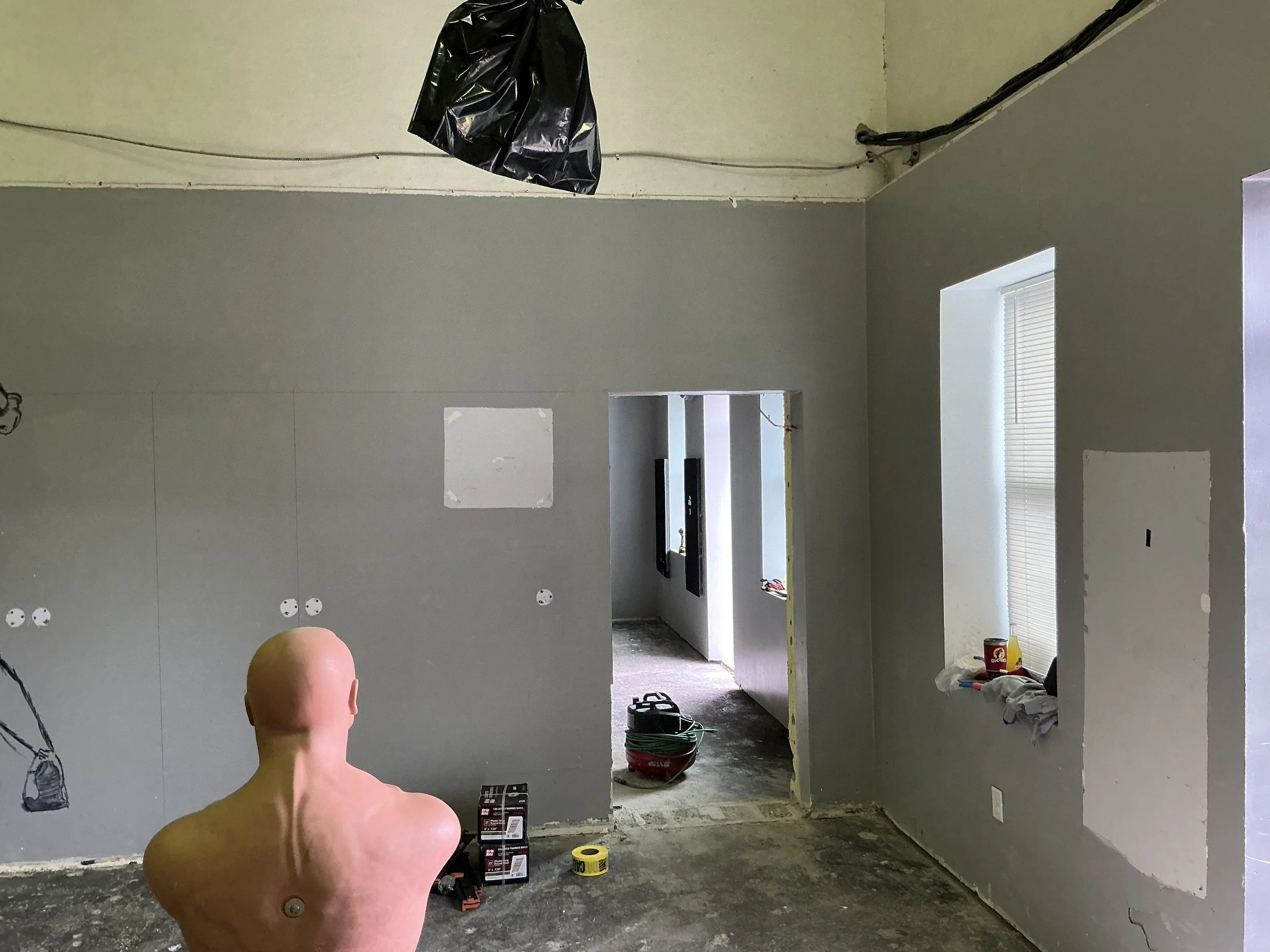 Empty room under renovation with drywall partially installed, construction tools, and a mannequin head in the foreground.
