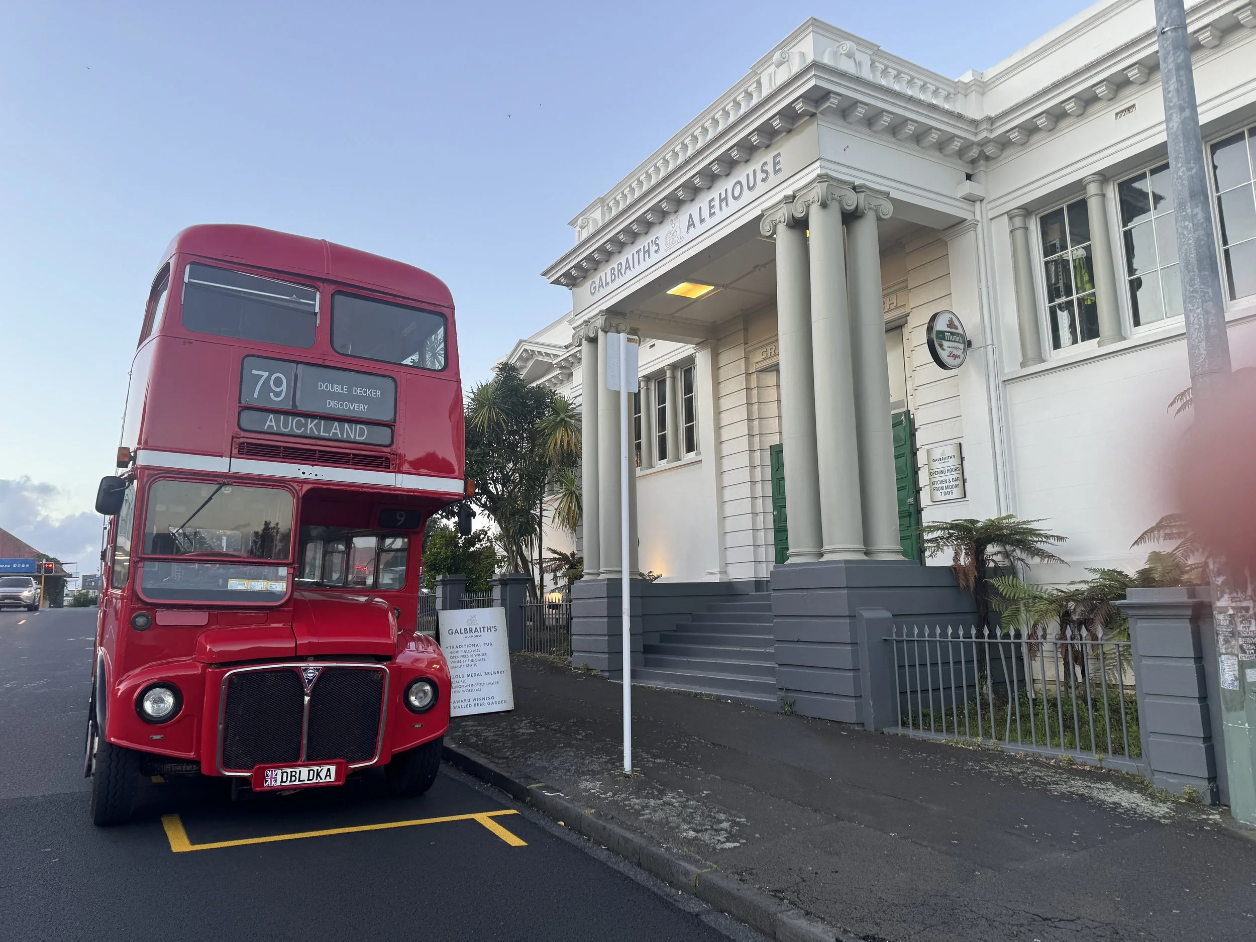 A vintage red double-decker bus parked next to the Galbraith's Alehouse building in Auckland, New Zealand.