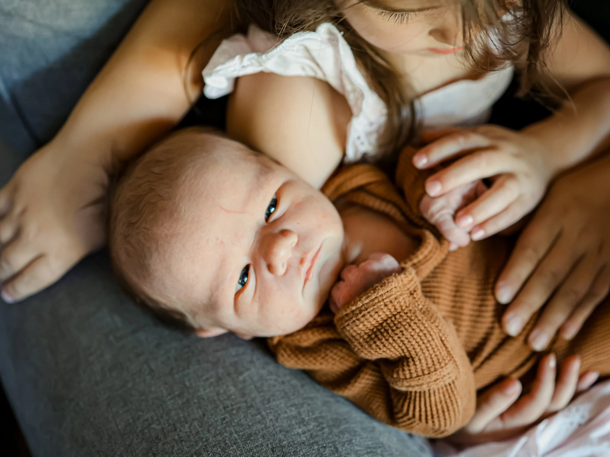 A woman feeding a newborn baby with a bottle while lying on a gray couch.