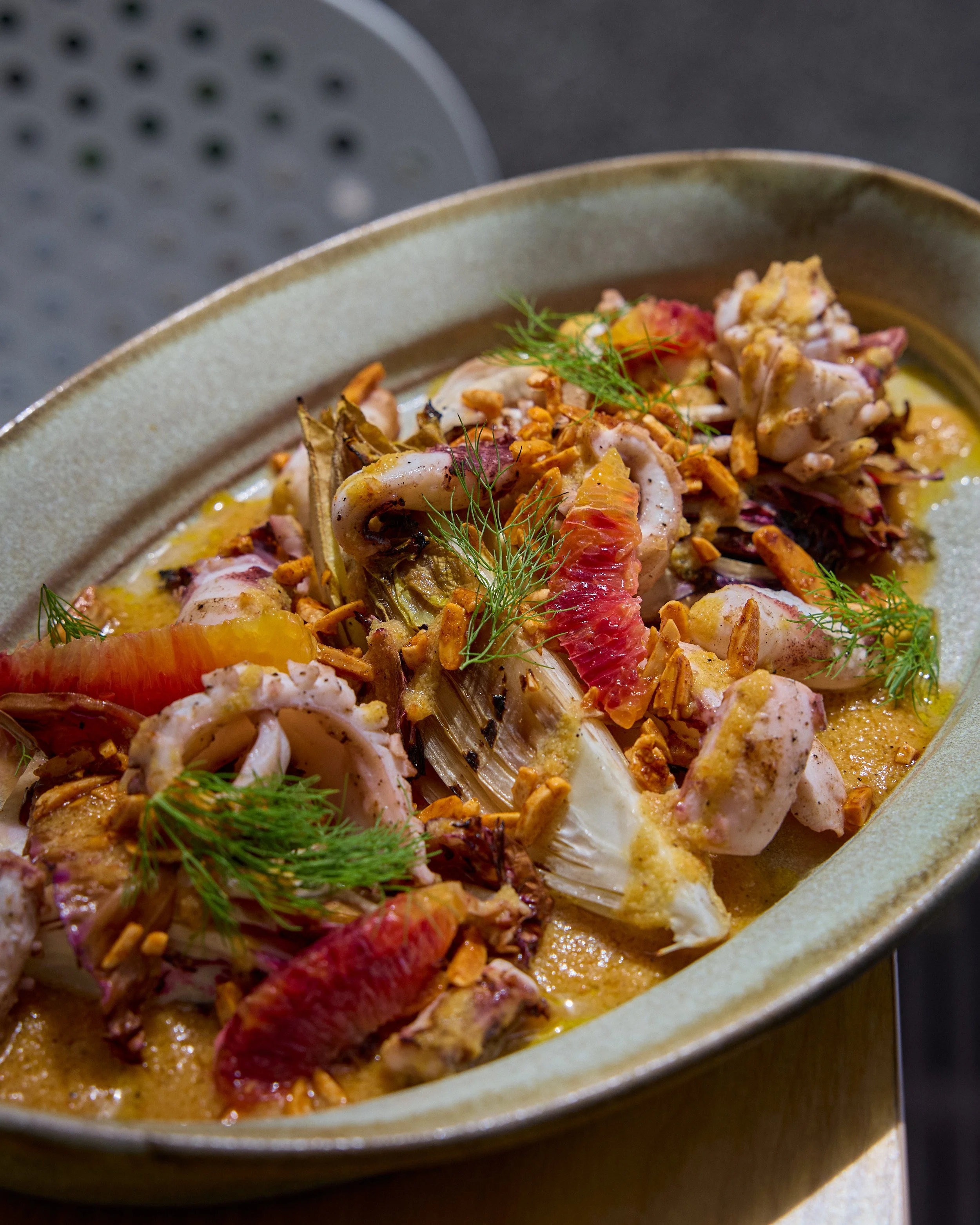 Close-up of a seafood dish in a beige bowl, featuring crab, garnished with dill and crunchy toppings.