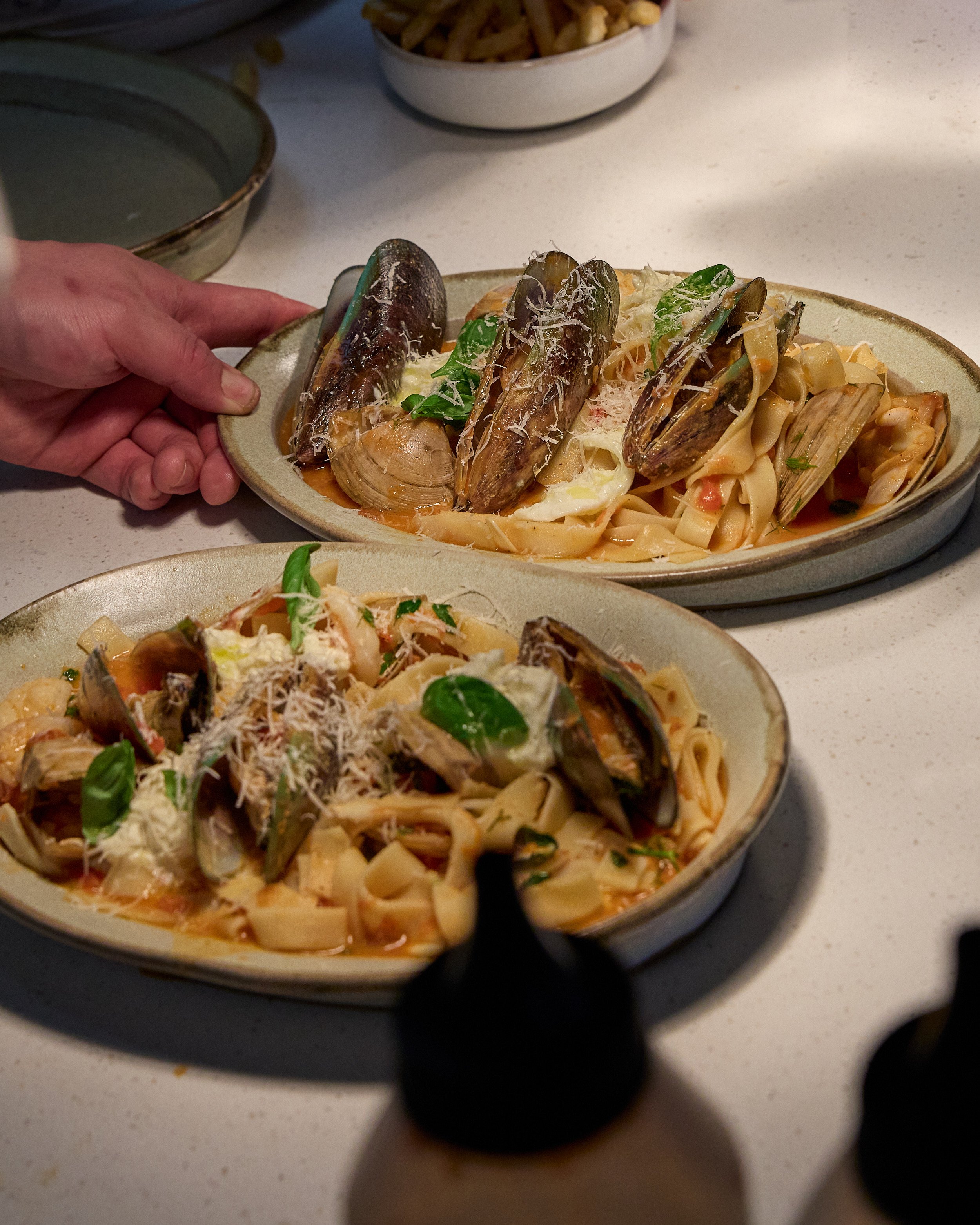 Plate of pasta with mussels, basil, grated cheese, and tomato sauce, with a hand holding the plate.