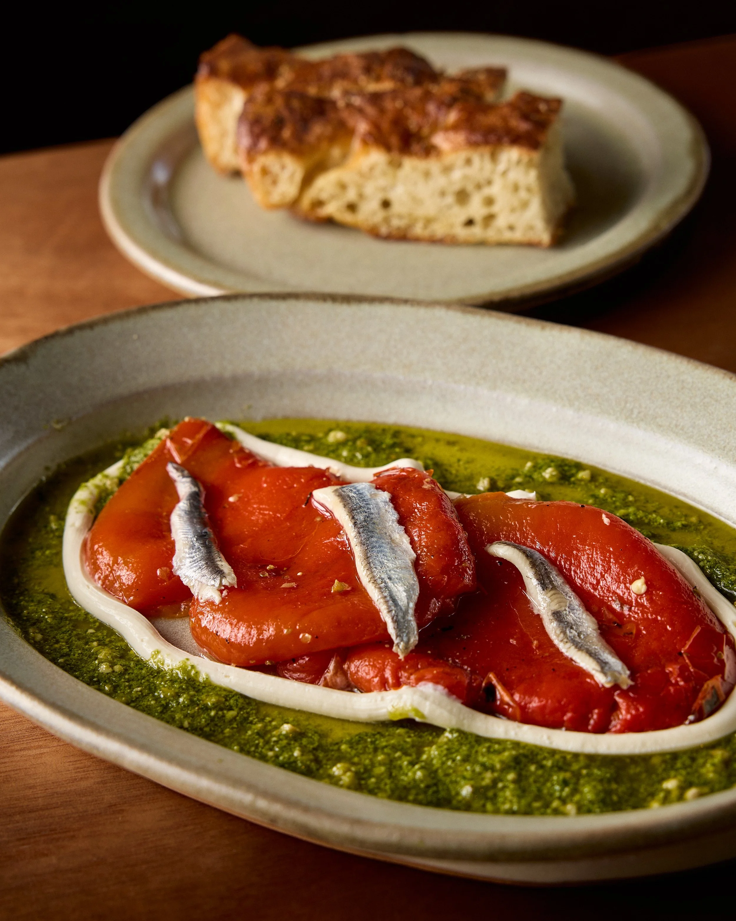 A dish of cured red fish, likely salmon, garnished with small fish fillets, served in a white oval dish with green sauce underneath.