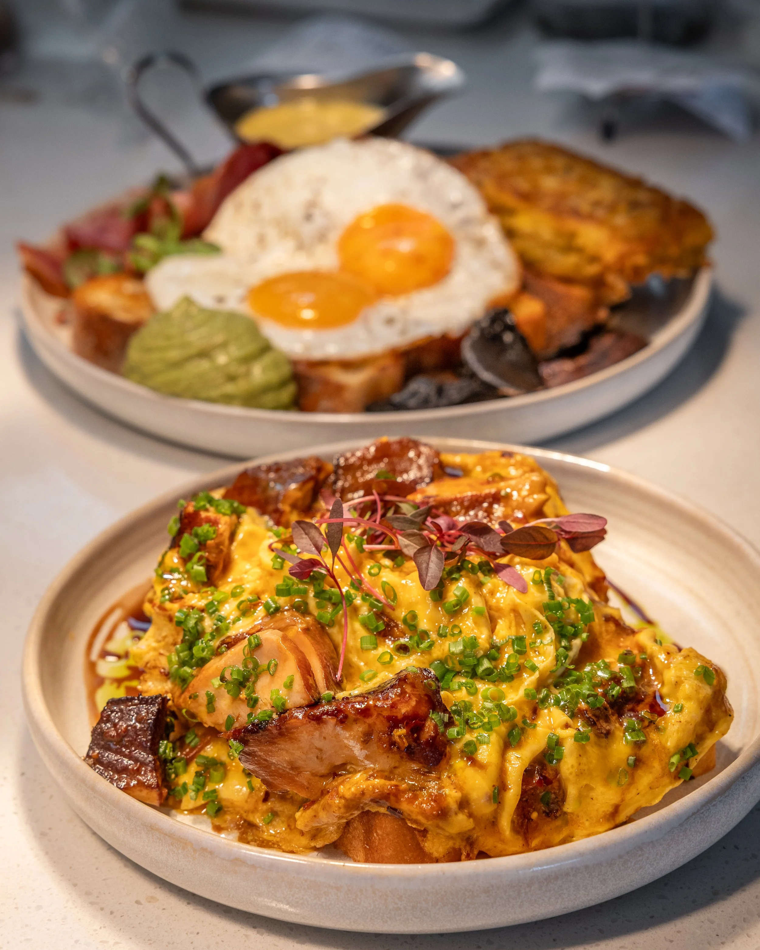 A bowl of food containing eggs, sliced meat, chopped herbs, and various other ingredients, set on a white surface.