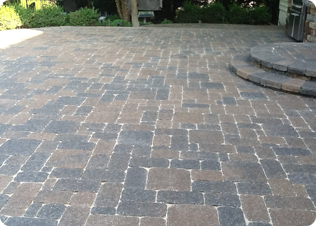 A paved patio area with a circular stone staircase on the right, outdoors with trees and greenery in the background.
