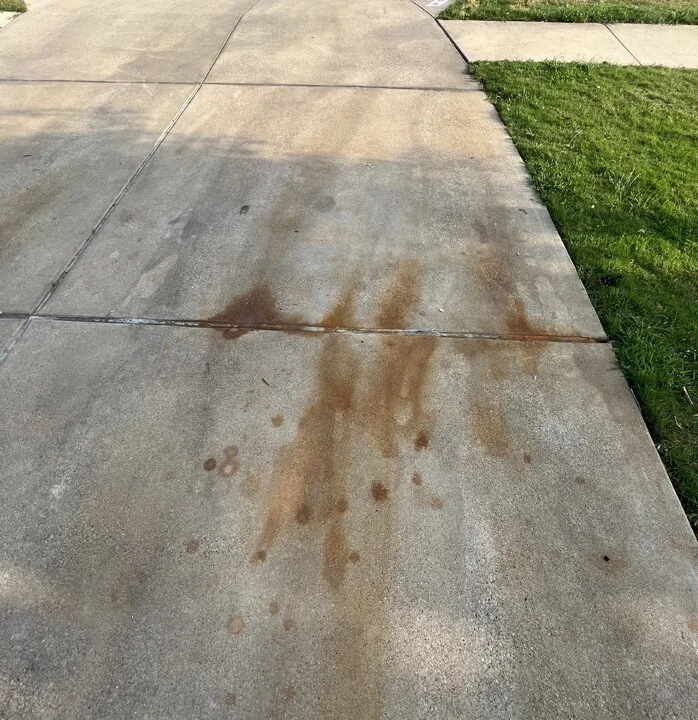 Concrete sidewalk with brownish stains and some grass on the side.