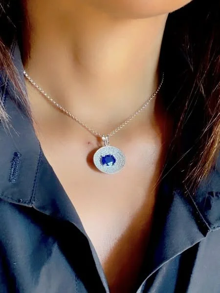 Close-up of a woman wearing a silver necklace with a blue gemstone pendant, dressed in a dark shirt.