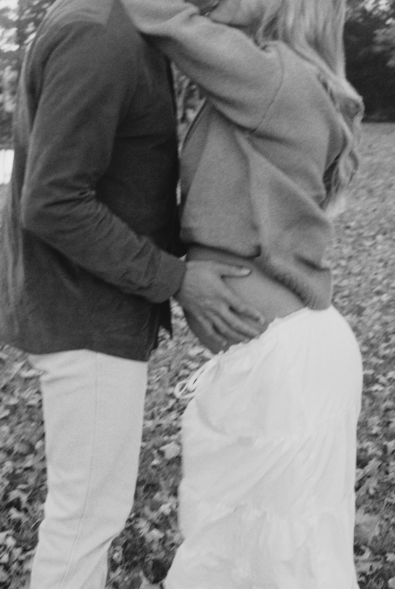 A couple sharing a kiss outdoors, with the woman holding her pregnant belly.