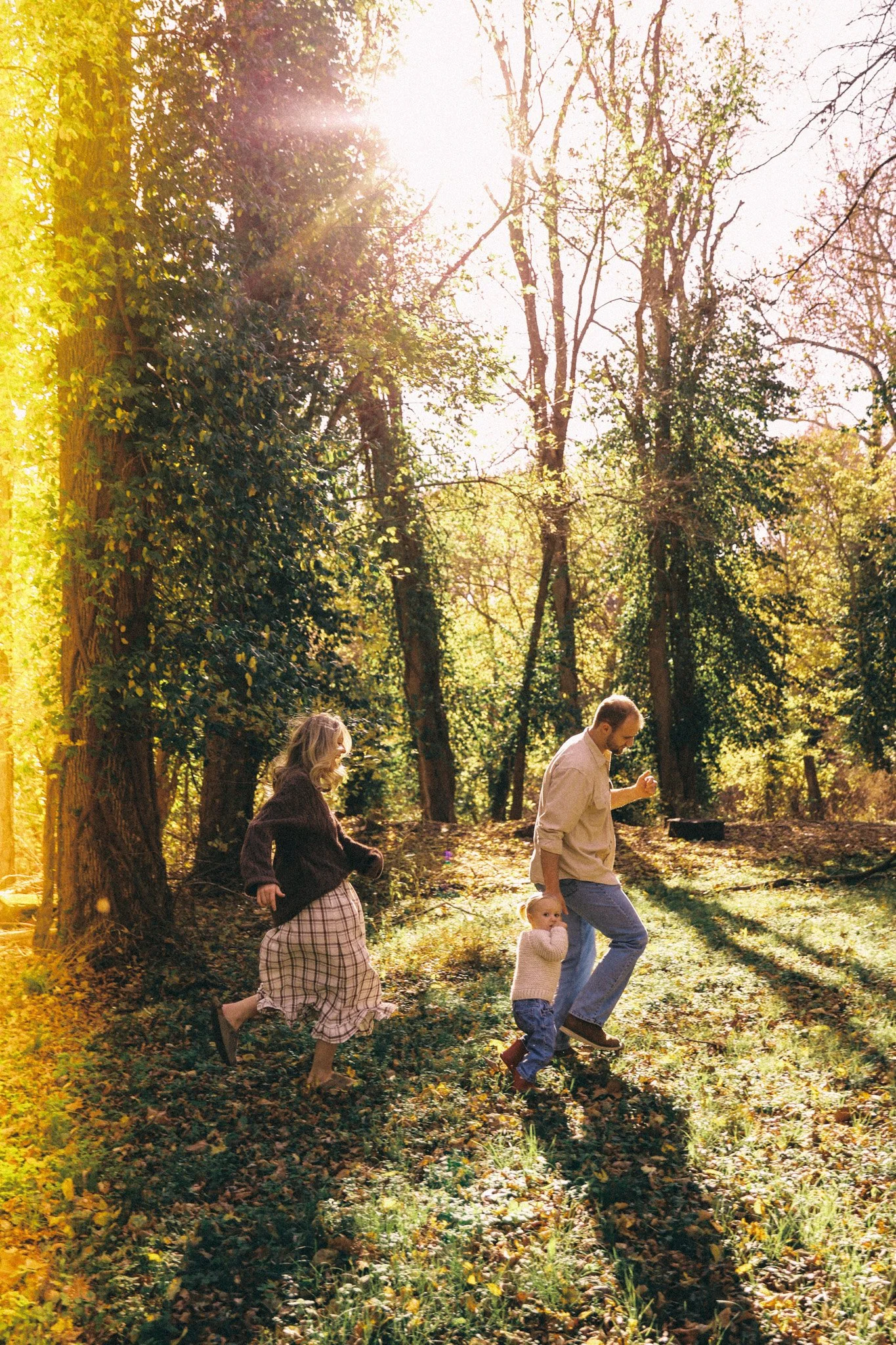 A family with a man, a woman, and two children playing outdoors in a wooded area during sunlight.