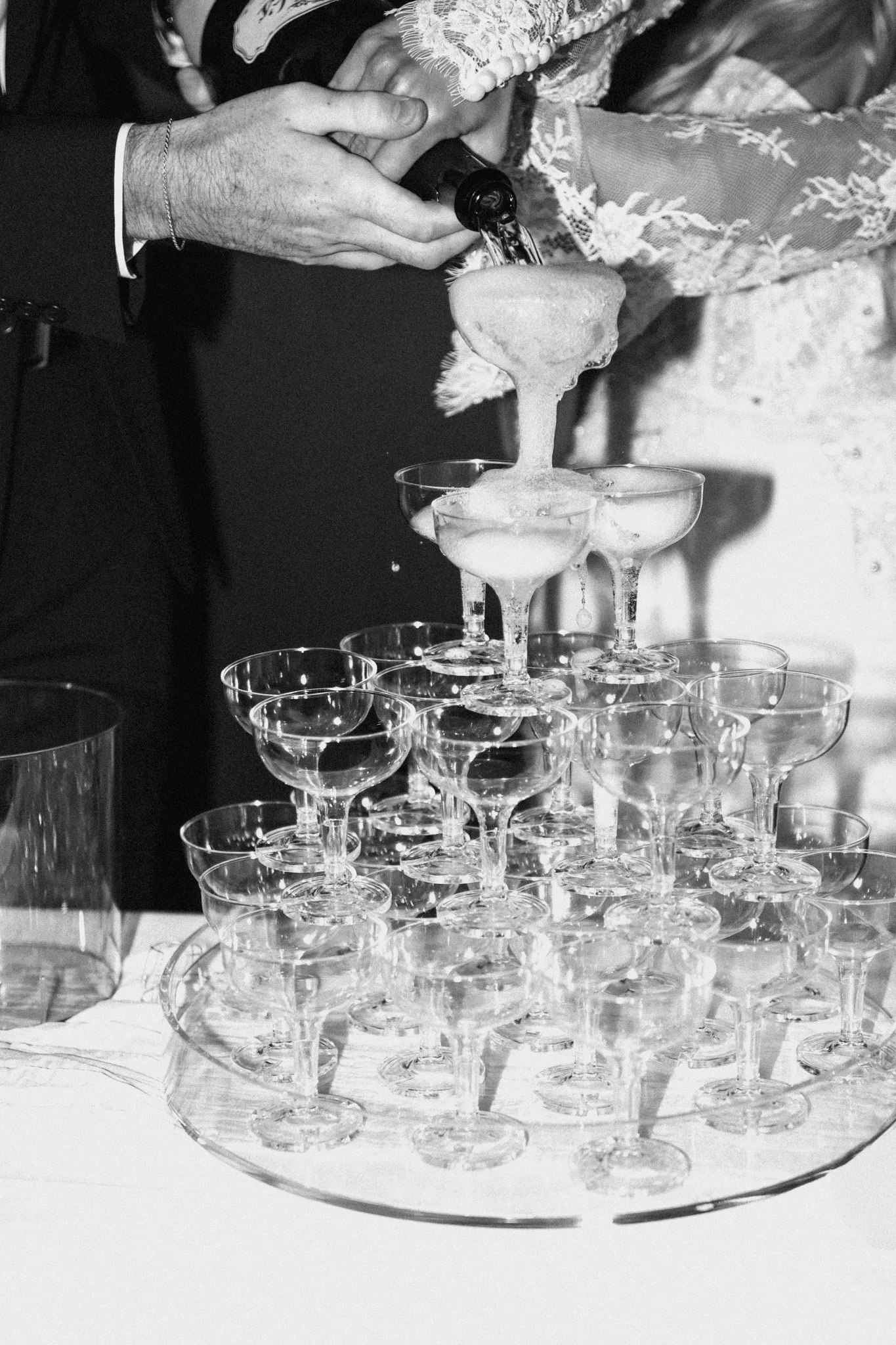 A person pouring champagne into a pyramid of empty glasses at a celebration event.