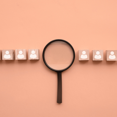 Wooden blocks with people icons under a magnifying glass, representing a broken candidate experience with confusing processes and unclear communication.