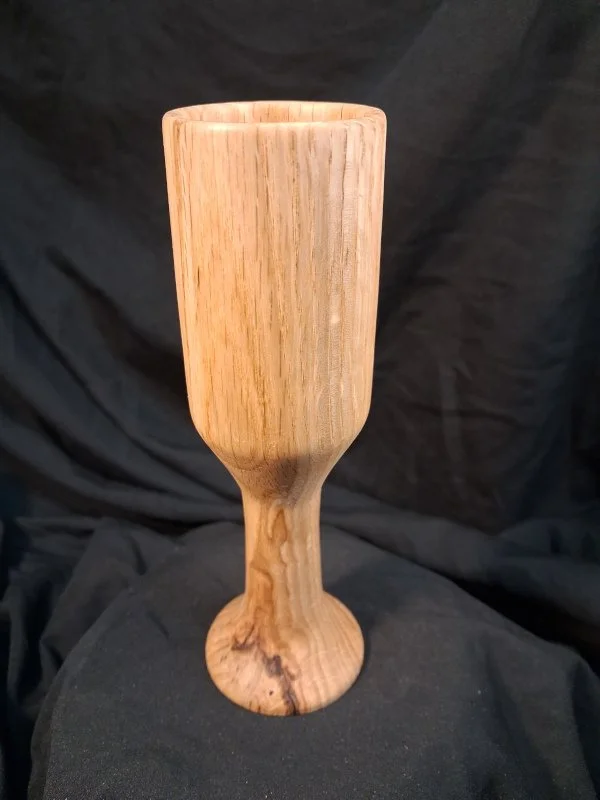Wooden goblet or chalice with a smooth finish, placed on a black fabric background.