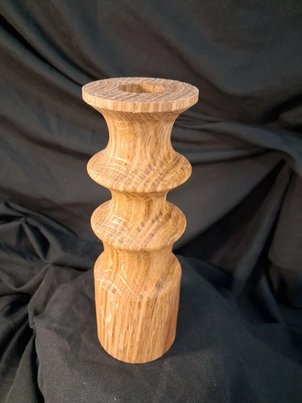 A wooden candlestick holder with a turned design, placed on a black fabric background.