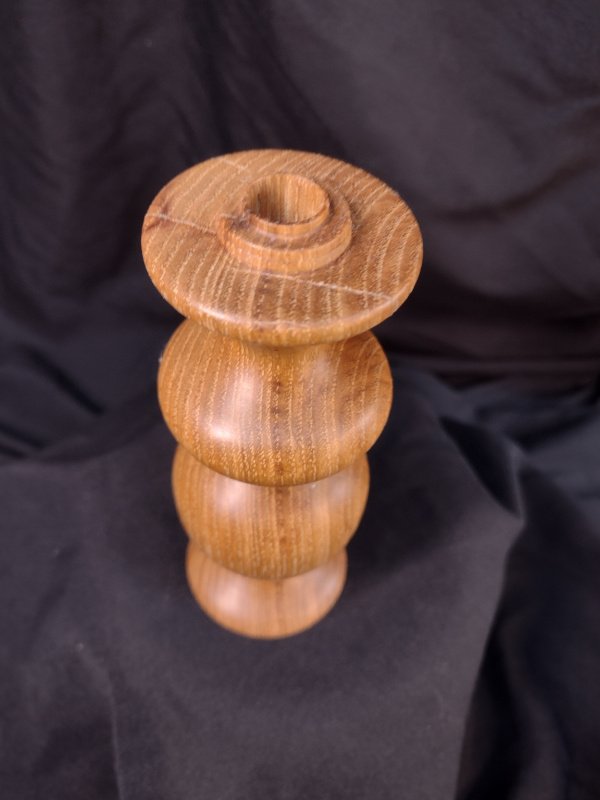 A wooden sculpture composed of stacked rounded cylindrical segments with a circular top, set against a dark fabric background.