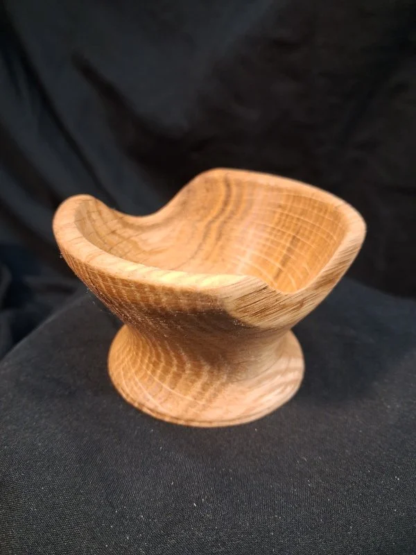 A small carved wooden bowl with a smooth finish, resting on a dark fabric surface.