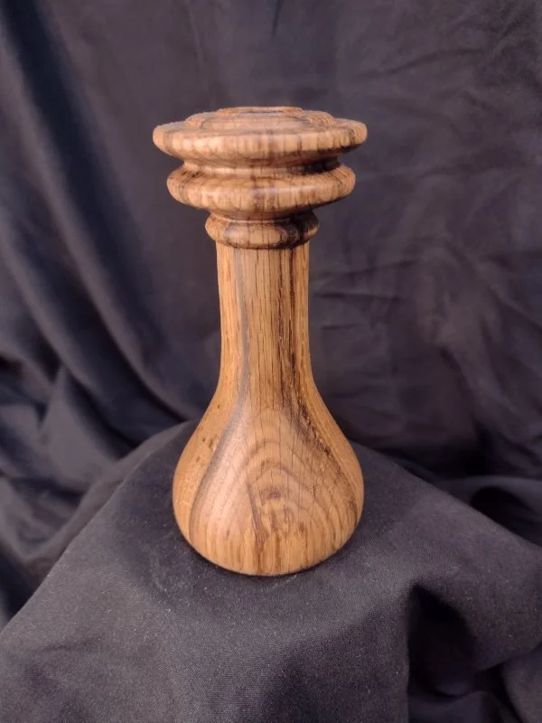 Wooden sculpture with a rounded base, a central hole and a carved top resembling a stylized vase or abstract art piece.