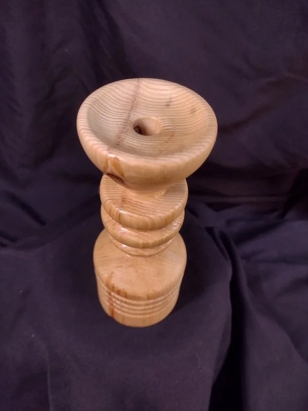 Stack of four wooden bowls or cups with the top one having a hole in the center, set against a dark fabric background.