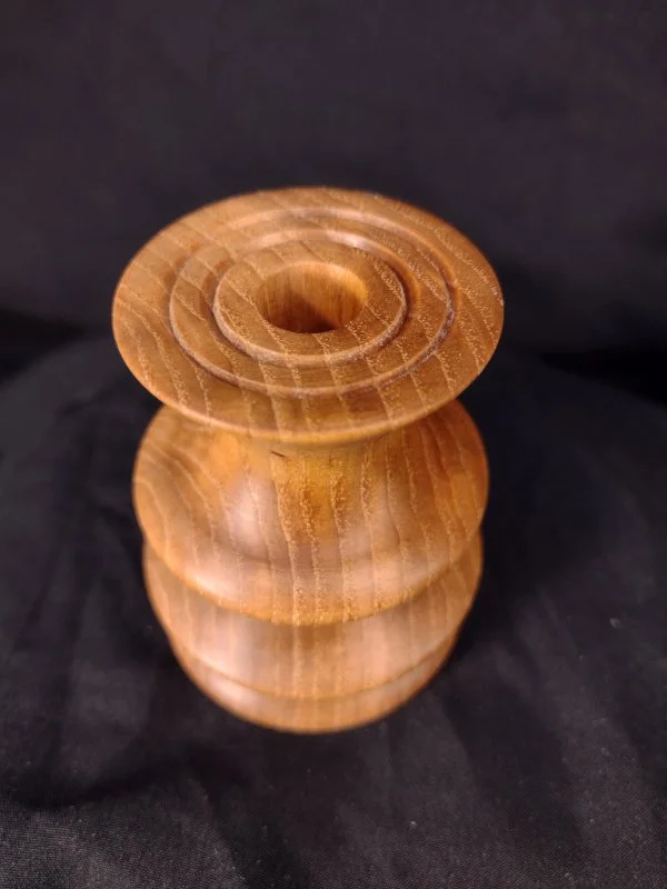 A wooden spool or reel with a central hole, displayed against a dark background.