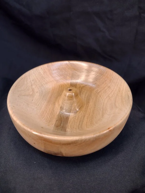 A wooden bowl with a small central spout, placed on a black background.