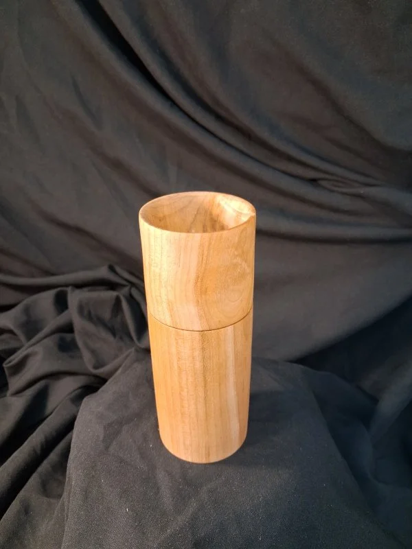 A wooden cylindrical container with a removable lid, placed on black fabric background.