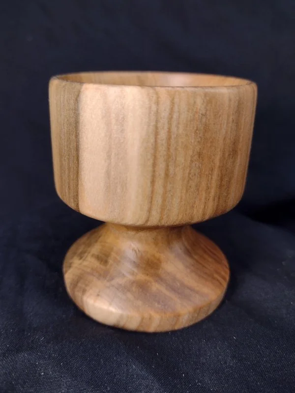 A wooden goblet with a rounded bowl and pedestal base, set against a black background.