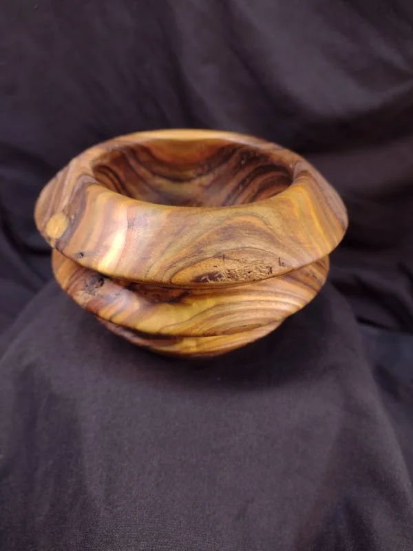 A wooden bowl with natural wood grain patterns, placed against a dark fabric background.