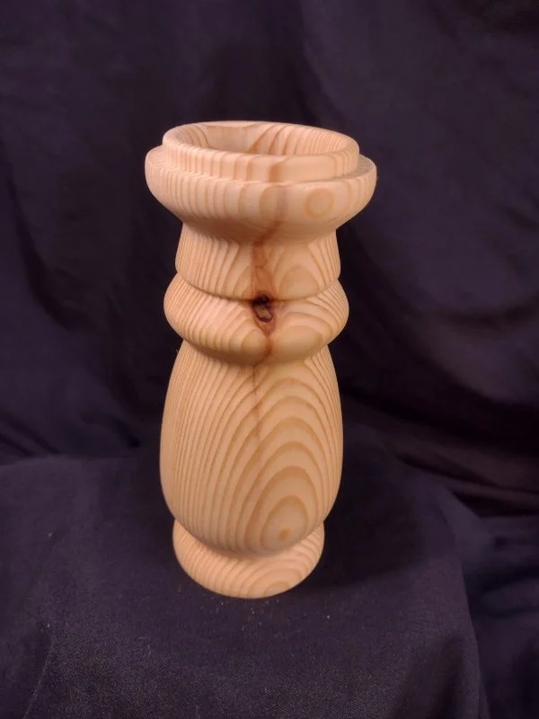 Wooden carved vase with a layered, curved design against a dark background.