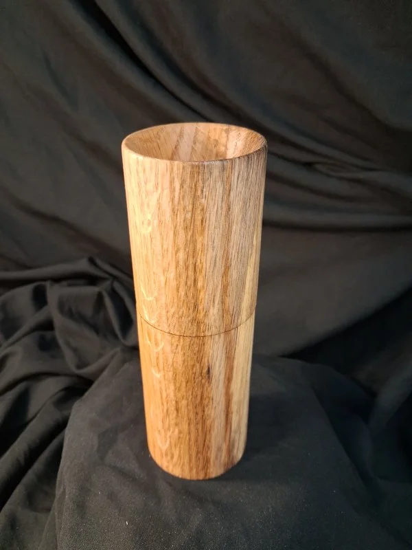 A wooden cylindrical container or beaker with a smooth surface, set against a dark fabric background.