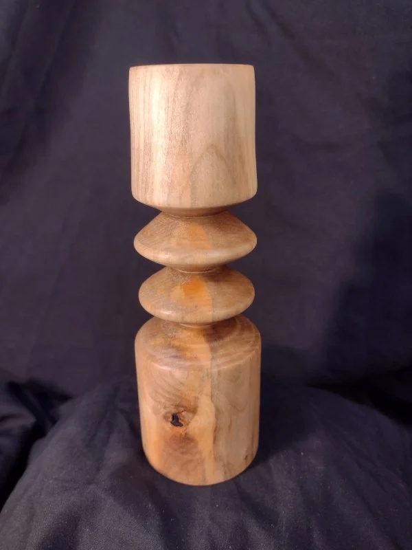 A wooden sculpture with a natural finish, featuring a tall, cylindrical top, three rounded, disc-shaped middle sections, and a shorter, rounded base.