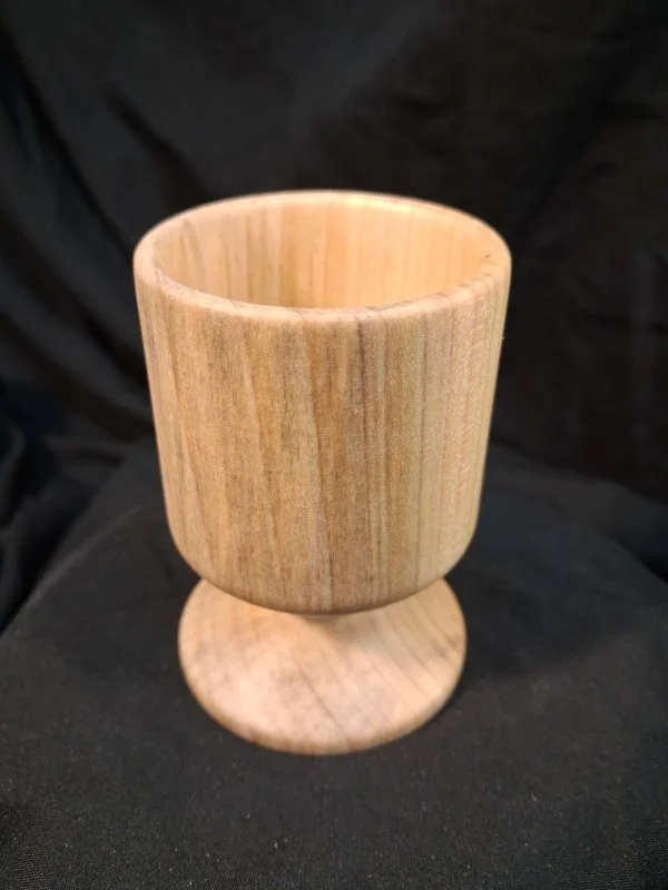 A wooden goblet with a rounded bowl and a circular base, made from light-colored wood with visible grain.