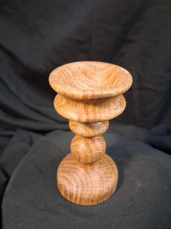 Wooden decorative stand with a bowl on top, made of carved wood, against a black background.