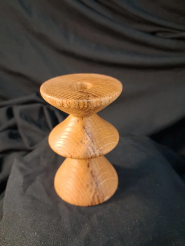 Wooden candle holder with a unique rounded design, placed on black fabric background.