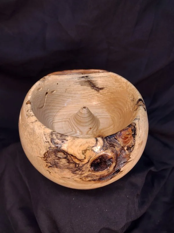 A small, round, wooden bowl with natural wood grain and knots, sitting on a dark fabric background.