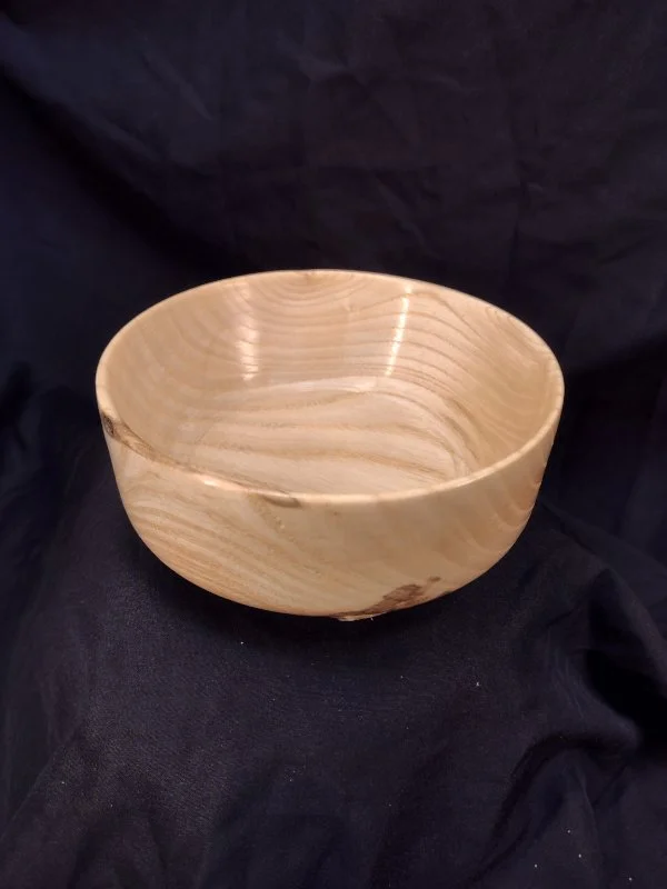 A wooden bowl with a smooth finish and natural wood grain, placed on black fabric.