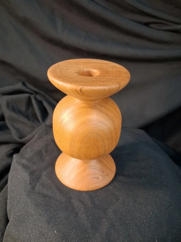 A wooden balancing sculpture with three rounded parts stacked vertically on a black fabric surface.