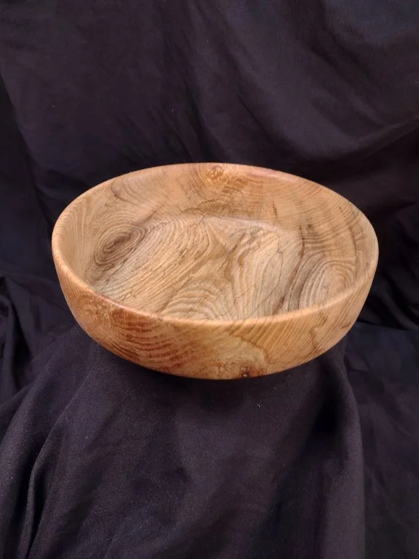 A wooden bowl with a natural finish, sitting on black fabric.