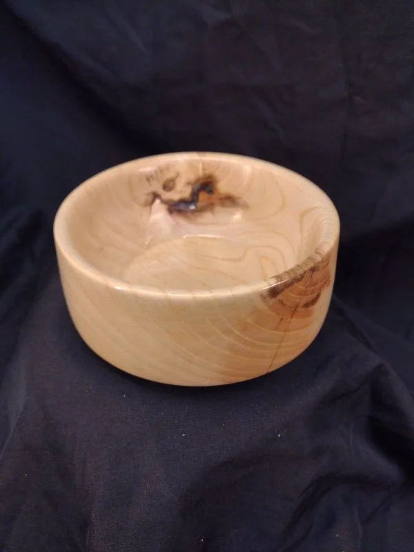 A round wooden bowl with a natural wood grain pattern, sitting on a black fabric surface.