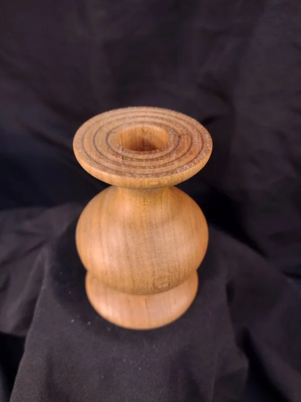 A wooden candle holder or small decorative stand with a rounded base and a flat, circular top with concentric rings.