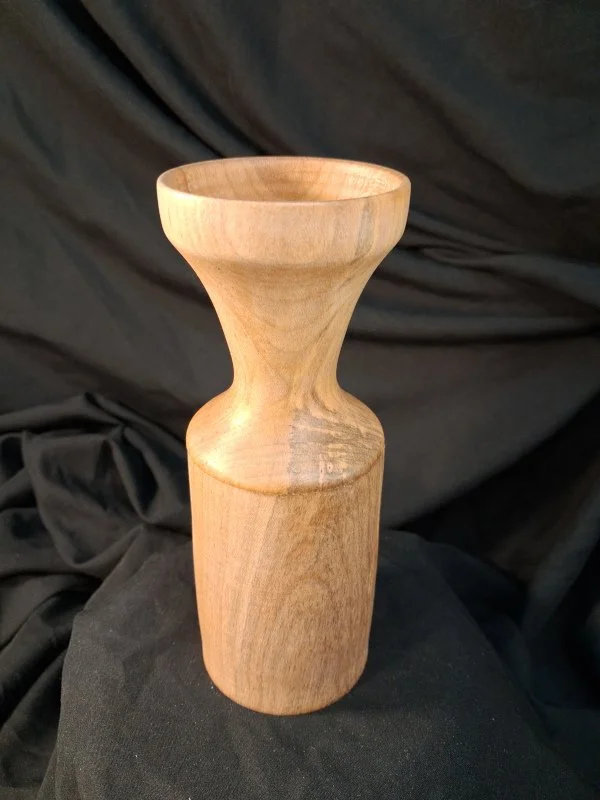 Wooden vase with a narrow neck and wide opening, placed on a black fabric background.