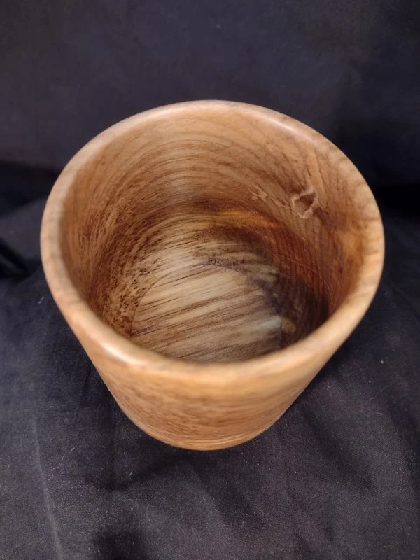 Close-up of a wooden cup on a black fabric background.